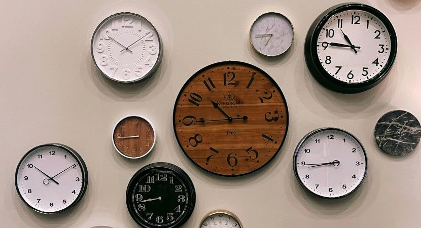 A selection of different clocks showing different times on a cream wall 